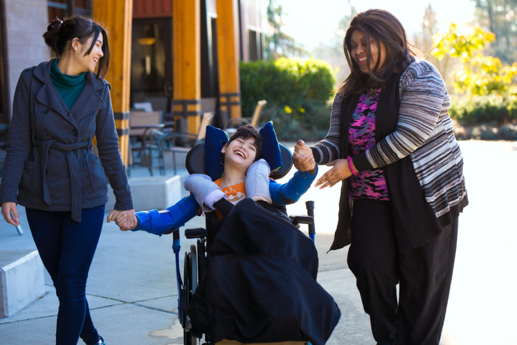 two women holding hands with little boy in wheelchair