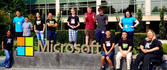 students posing for a photo. They are all seen standing around a physical microsoft logo at the microsoft campus.
