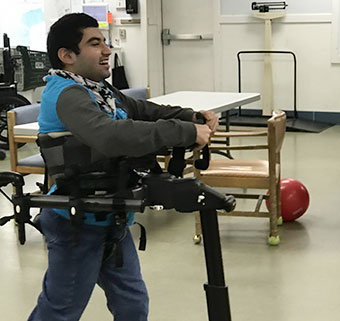 A teenager using the Rifton Pacer gait trainer to walk in a classroom.