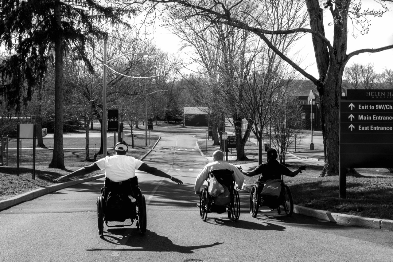 Three men in manual wheelchairs rolling down a hill on an empty street, taken by disabled photographer Nolan Ryan Trowe