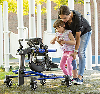 A therapist helps a young girl into a gait trainer.